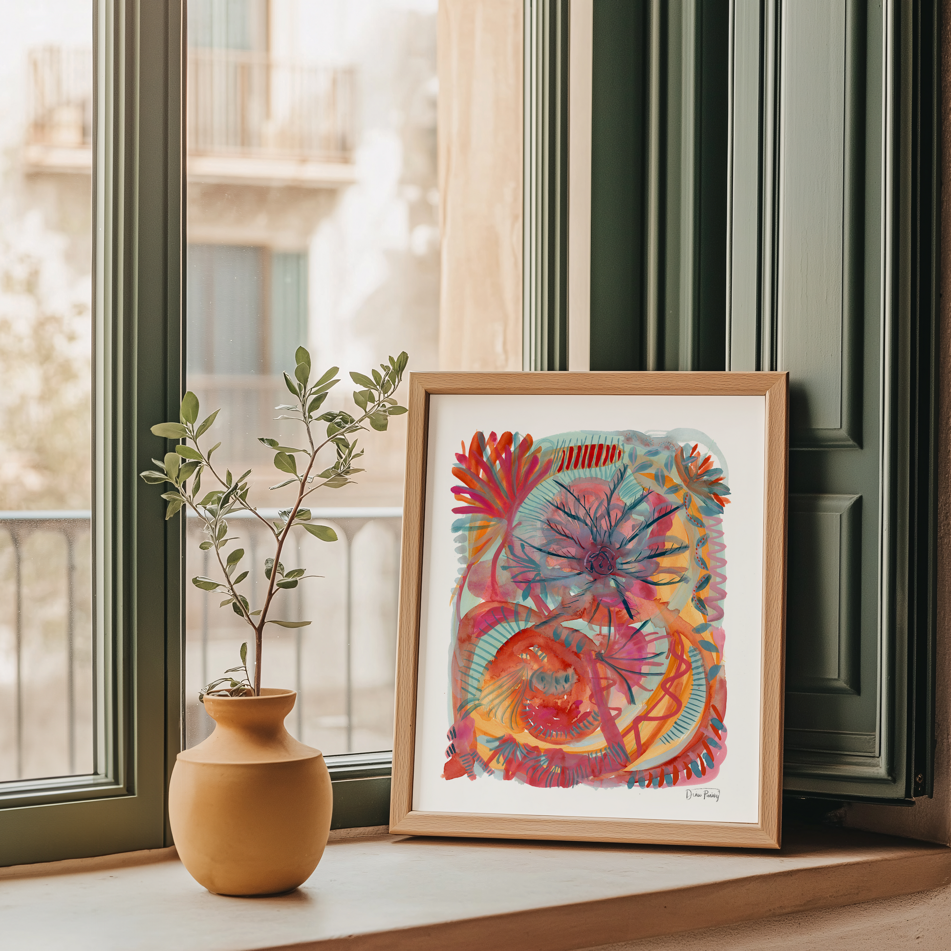 A framed abstract art print with a colorful floral pattern in red, orange, blue, and pink, displayed on a windowsill next to a small terracotta vase with a plant.